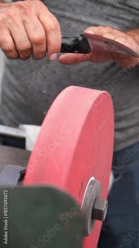 Man sharpens knife with grinding wheel in workshop