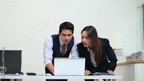 Two  Asian businessman and woman workers talking on the smartphone and using laptop Professionals in Teamwork Finance, Marketing, and Success at the office.