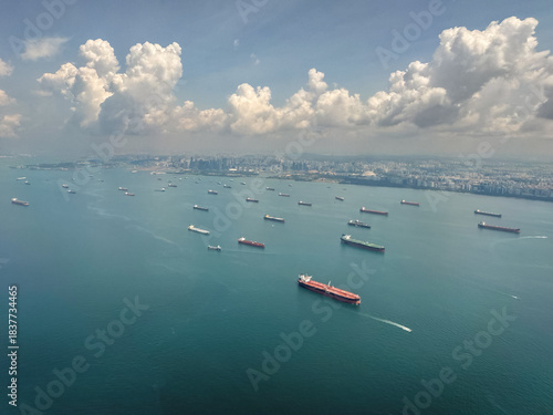 View of numerous cargo ships in the waters near a coastal city with scattered clouds