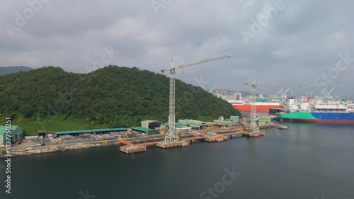 Aerial view of a dynamic shipbuilding yard featuring large vessels, numerous towering cranes, and industrial structures, capturing busy maritime construction operations.