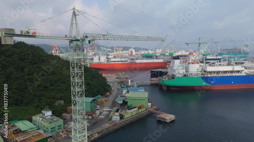 Aerial view of a busy shipyard with massive cargo and LNG ships under construction, surrounded by towering cranes and industrial facilities, showcasing the impressive scale of modern shipbuilding and 