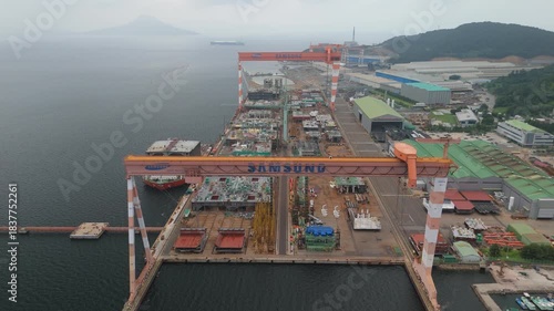 Aerial shot of a vast shipyard, featuring immense gantry cranes and ships under construction. A dynamic industrial scene showcasing shipbuilding operations and maritime manufacturing by the sea.