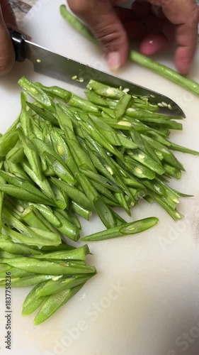 Hand movement of a bean cutter with a sharp knife on a white chopping board