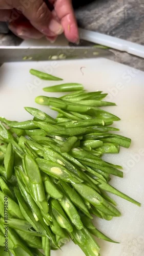 Hand movement of a bean cutter with a sharp knife on a white chopping board