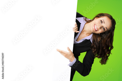 Happy smile cute brunette haired woman peep out show pointing advertise blank white banner signboard with empty sign text free space, isolated vivid green background. Business ad concept