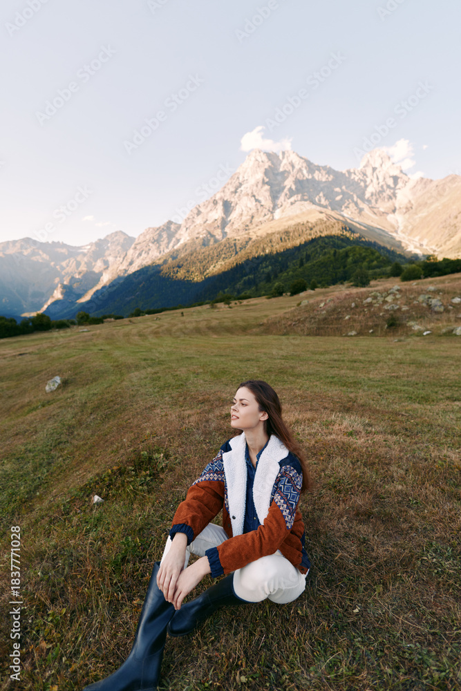 Obraz premium Woman sitting in meadow with mountains behind, portrait of travel and nature scene in autumn, cozy sweater and peaceful landscape for outdoor leisure and scenic horizon.