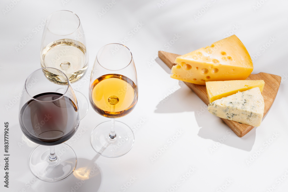 Fototapeta premium Assorted cheeses and wine glasses on white background