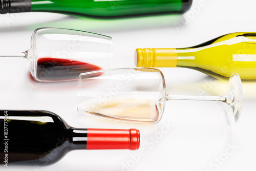 Wine glasses with red and white wine and bottles lying on white background