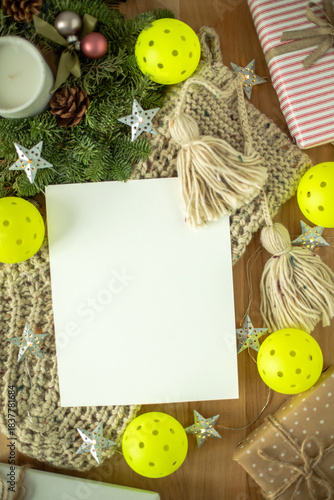 Festive flat lay with blank paper, Christmas gifts, yarn tassels, stars, greenery, and bright pickleballs. Perfect for holiday cards, winter designs, and seasonal invitations.