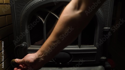 Hand closing the door of a fireplace stove, close-up in a dark room