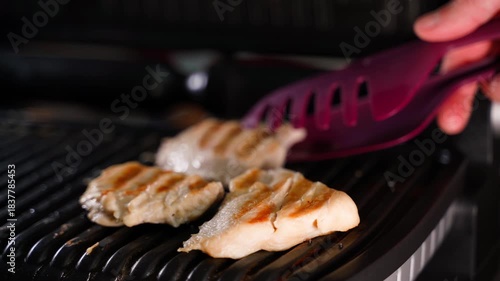 Grilled chicken fillet being removed from electric grill with tongs, close-up