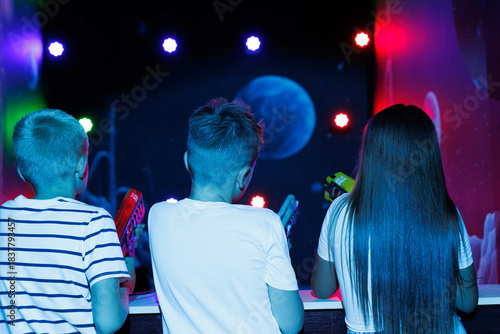 Two boys and a girl playing laser tag in a dark room with bright lights and a planet projection.