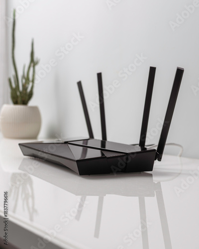 Sleek WIFI router with four antennas on white desk near cactus in pot, minimalist home interior for wireless internet connection.