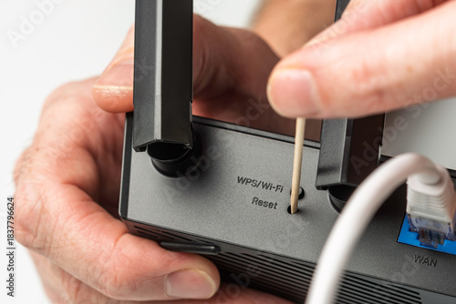 Canvas Print Closeup of hand resetting WiFi router with toothpick through WPS reset hole duri