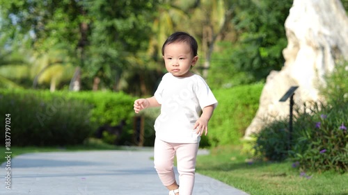 A little girl just over 1 year old learning to walk in the park with the evening light giving a warm feeling