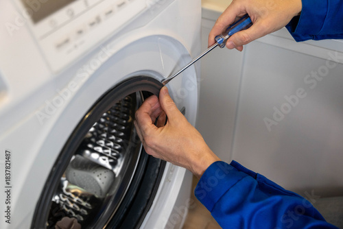 Worker fixes washing machine door seal in a laundry room during the afternoon