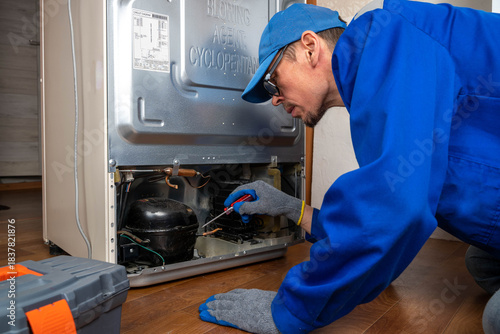 Man repairs refrigerator at home in morning with tools and focused attention