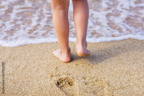 Child's feet standing on the sand at the edge of the sea