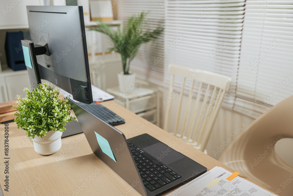 Fototapeta premium Modern home office workspace presents laptop computer desk for business with monitor, organized papers, green plant, bright blinds, creating comfortable environment for remote work, study or project