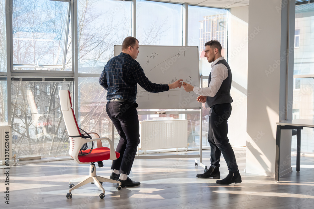 Fototapeta premium Two Caucasian men discussing work at a white board. 