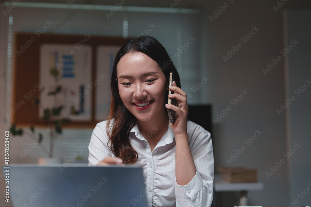 Fototapeta premium Woman talking on phone and working using laptop
