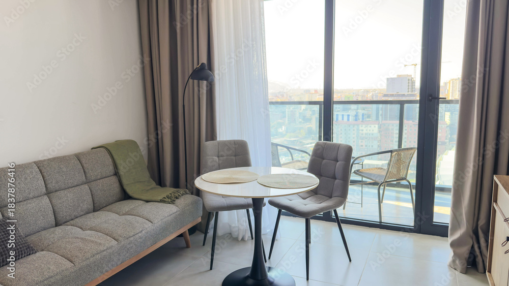 Fototapeta premium Modern cozy living room with soft neutral tones, round dining table and panoramic balcony view