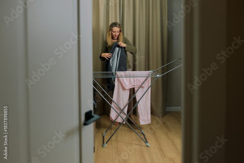 Woman is carefully folding freshly laundered clothes on a drying rack inside a cozy room