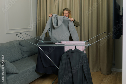 Woman hanging laundry indoors on a drying rack in a cozy living room