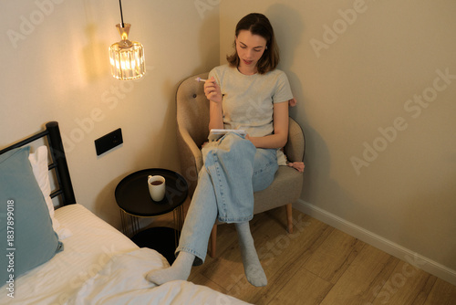 Woman relaxing in a cozy room while writing in a notebook and enjoying a cup of coffee