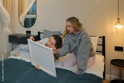 Two women creating art together in bedroom setting during evening hours