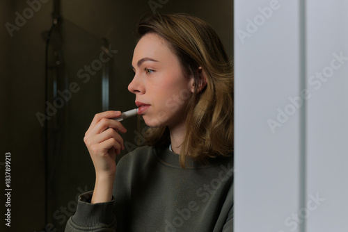 Woman applying lip balm in a cozy indoor setting, reflecting a moment of personal care and self-grooming