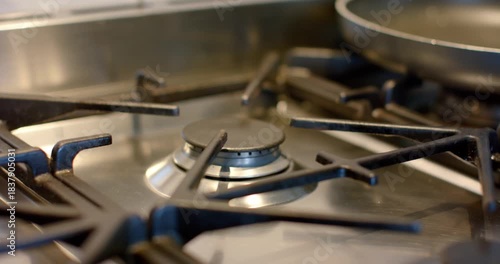 Offscreen turning knob in kitchen igniting stainless steel burner lighting blue flame heating pan