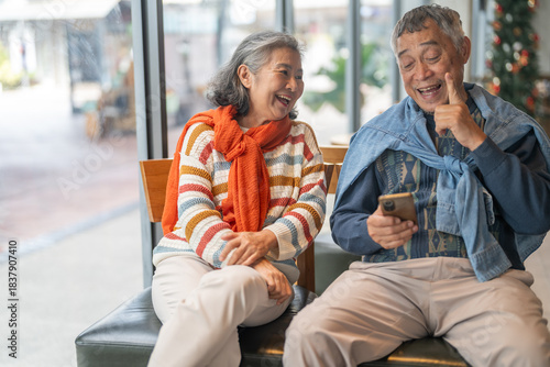 Senior asian couple using smartphone together sitting and smiling at cafe with digital technology, mobile banking, online shopping or telehealth services for elderly, modern lifestyle after retirement