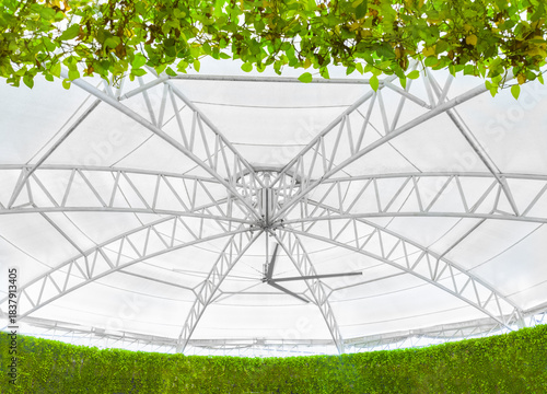 the structural steel framework that forms the main core of a modern dome-style fabric roof. It highlights both strength and contemporary design, surrounded by lush, vibrant greenery