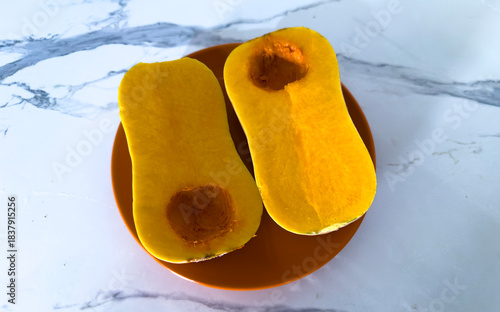 Halved butternut squash with seasoning on orange plate