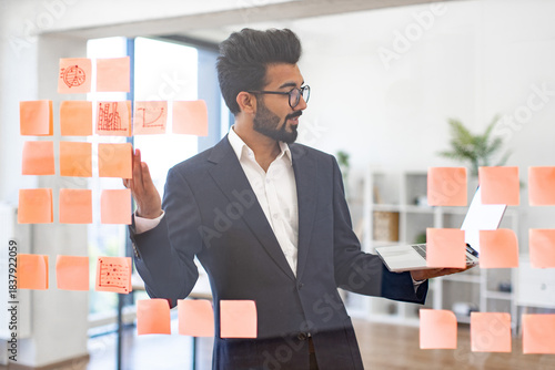 An Arabian businessman is working on a project with sticky notes and a laptop in a modern office setting