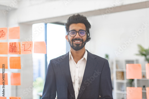 An Indian businessman wearing a headset smiles in a modern office setting