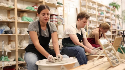 Female positive artisan in ceramics workshop with pottery wheel and various clay vessels. High quality 4k footage