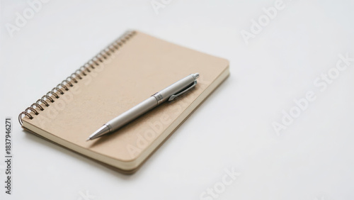 A spiral notebook with a metal pen rests on a light-toned background, conveying the simple and quiet atmosphere of writing and office scenes.