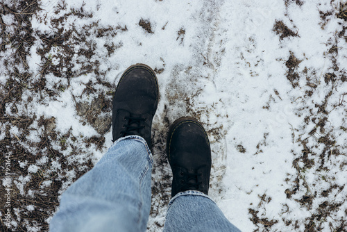 Female legs in black leather boots on icy surface. Winter injury and climate change concept. Winter boots, shoes, stands on the ground with snow in winter outdoors. Top view.