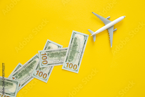 Toy airplane and dollar bills on yellow background, flat design. Vacation, air travel and air tickets concept.