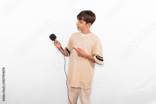 young casual dressed Generation Z influencer white male host model teenage boy with microphone for singing, presenting and interviewing for social media channel. plain background studio setting