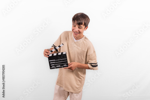 young happy casual dressed Generation Z influencer white male model teenage boy prepares to create and direct fun social media film reel with blank clapperboard slate. plain background studio setting