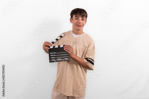 young happy casual dressed Generation Z influencer white male model teenage boy prepares to create and direct fun social media film reel with blank clapperboard slate. plain background studio setting