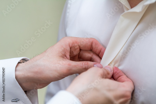 The best man helps the groom button his shirt during the wedding preparations. A helping hand, friendship, an important live moment.