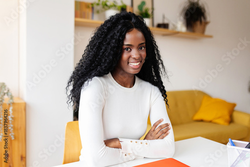 Portrait of young happy black woman with laptop smiling at camera sitting on table at home. Business and education concept