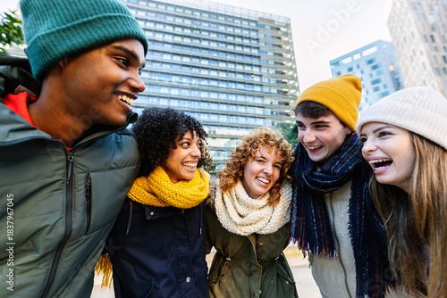 Group of young multiracial friends outdoors in a city during cold weather. Millennial tourists or students dressed warmly, having fun together outside. Friendship and winter lifestyle concept.