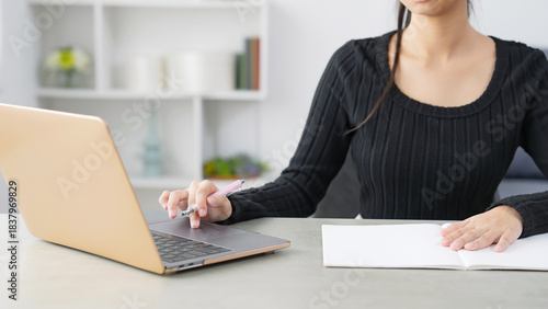 部屋でノートパソコンを見ながら勉強する女性