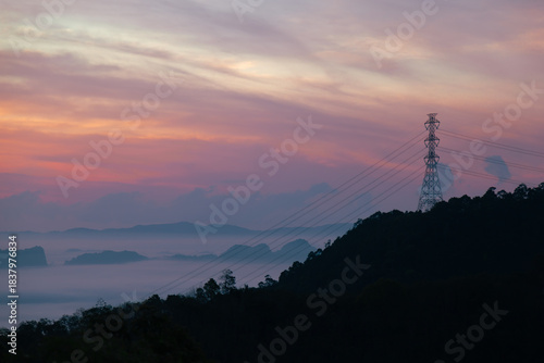 Power Transmission Tower Silhouette on a Hill with Beautiful Pink and Purple Sunrise Sky. Electric pylon contrasting nature and infrastructure.