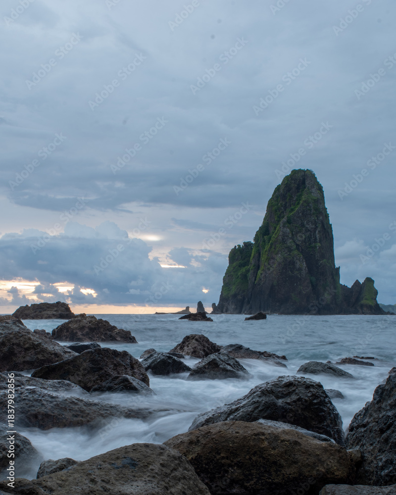 Naklejka premium Mystical seascape with dark volcanic rocks and tall sea stacks emerging from silky ocean water during twilight, show.casing serene coastal nature